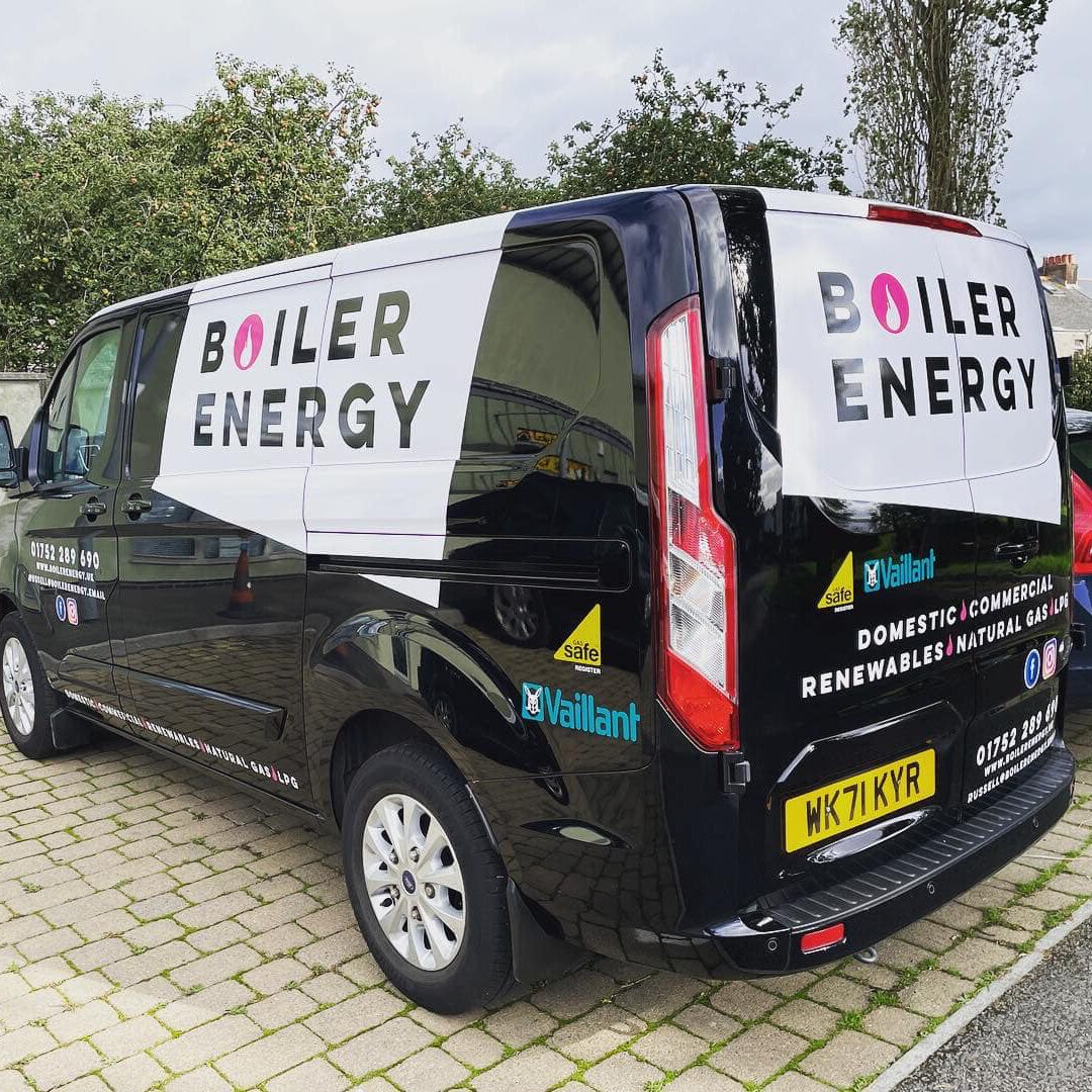 A black van parked on a paved area is boldly branded with "Boiler Energy." It offers services like gas central heating and heating system repairs for domestic, commercial, renewables, and natural gas. Trees and buildings frame the scene in the background.