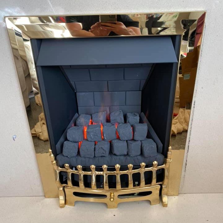 A modern fireplace with a metallic gold frame and artificial glowing coals mimics the warmth of a lit fire, perfect for when boiler upgrades or gas central heating are on the to-do list. The light-colored wall reflects someone capturing this comforting scene.