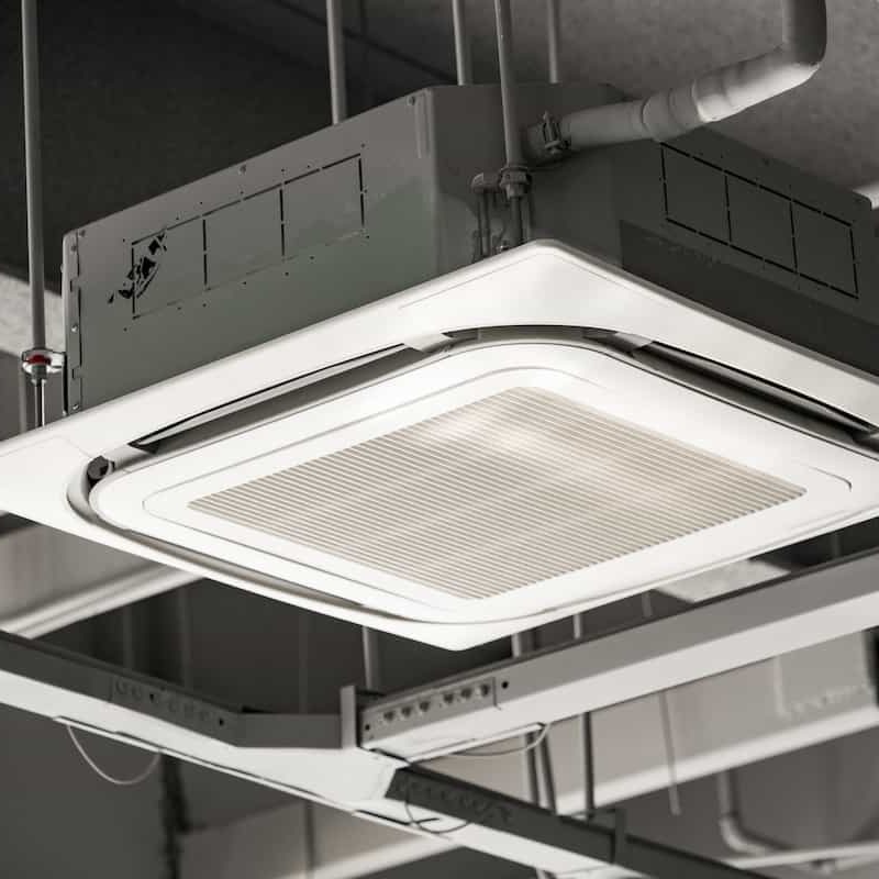 A ceiling-mounted air conditioning unit with vents, pipes, and cables attached, set in an industrial-style ceiling with exposed ductwork and metal beams.